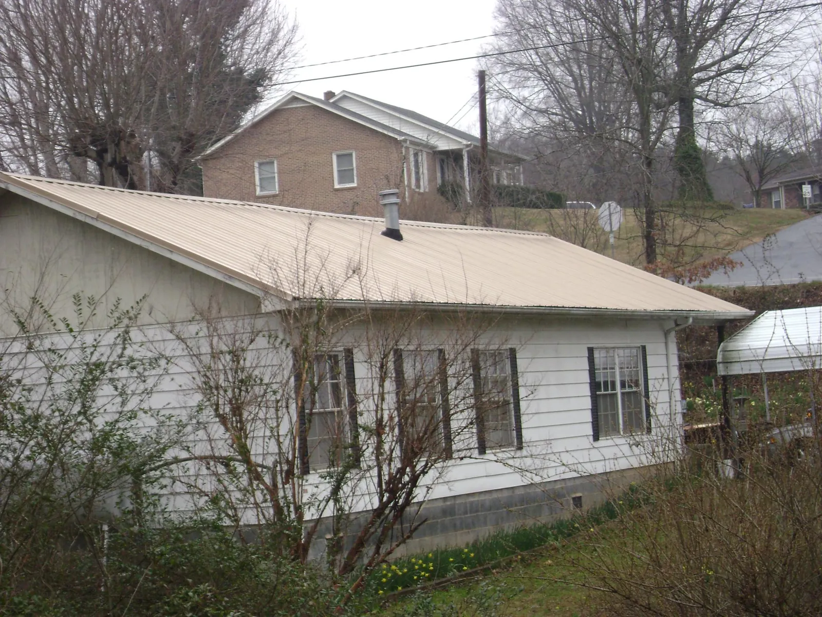 Tan metal roof on a white sided house set into a hillside — Commercial Roofing by Roofing Brothers in Reading